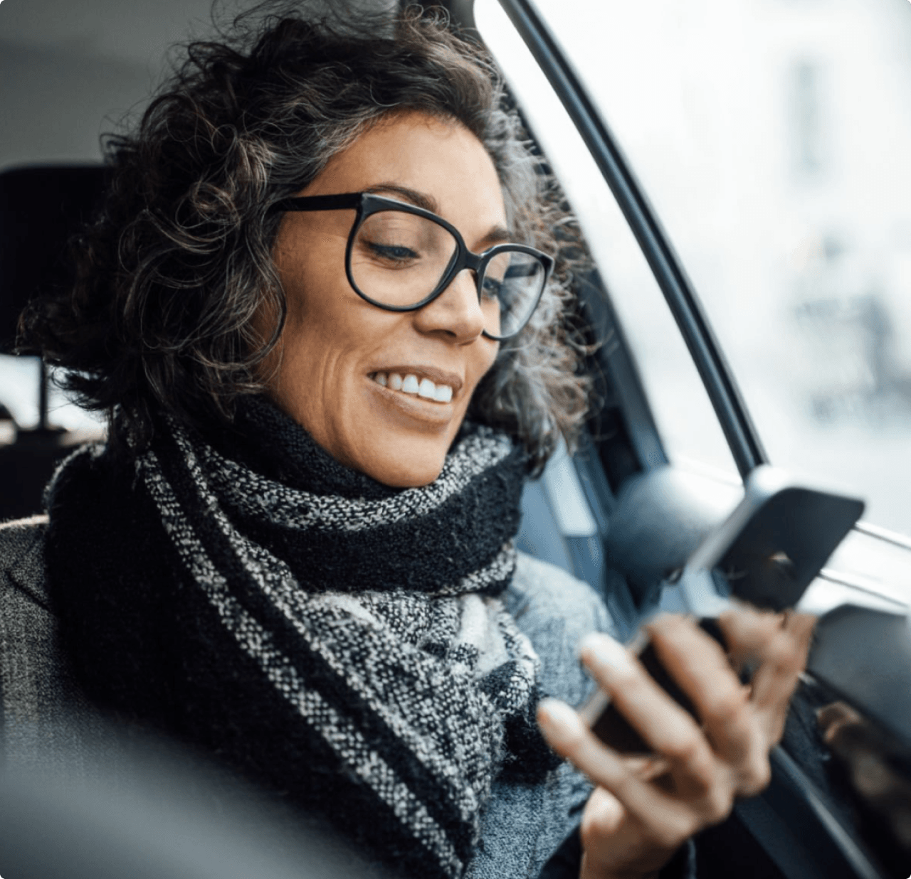 A middle aged woman in glasses, looking at her phone whilst in the passenger seat of a car